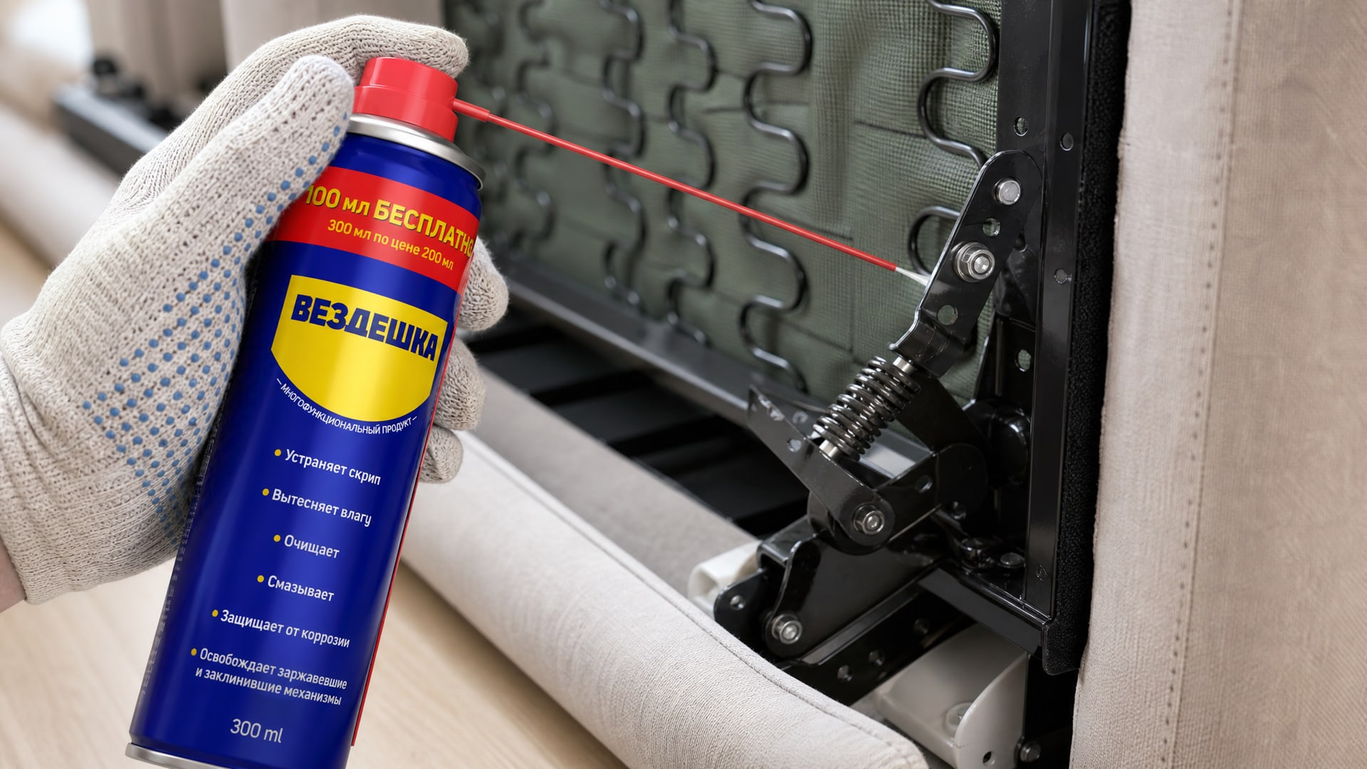 Рука в перчатке распыляет универсальную смазку WD-40 на детали дивана.