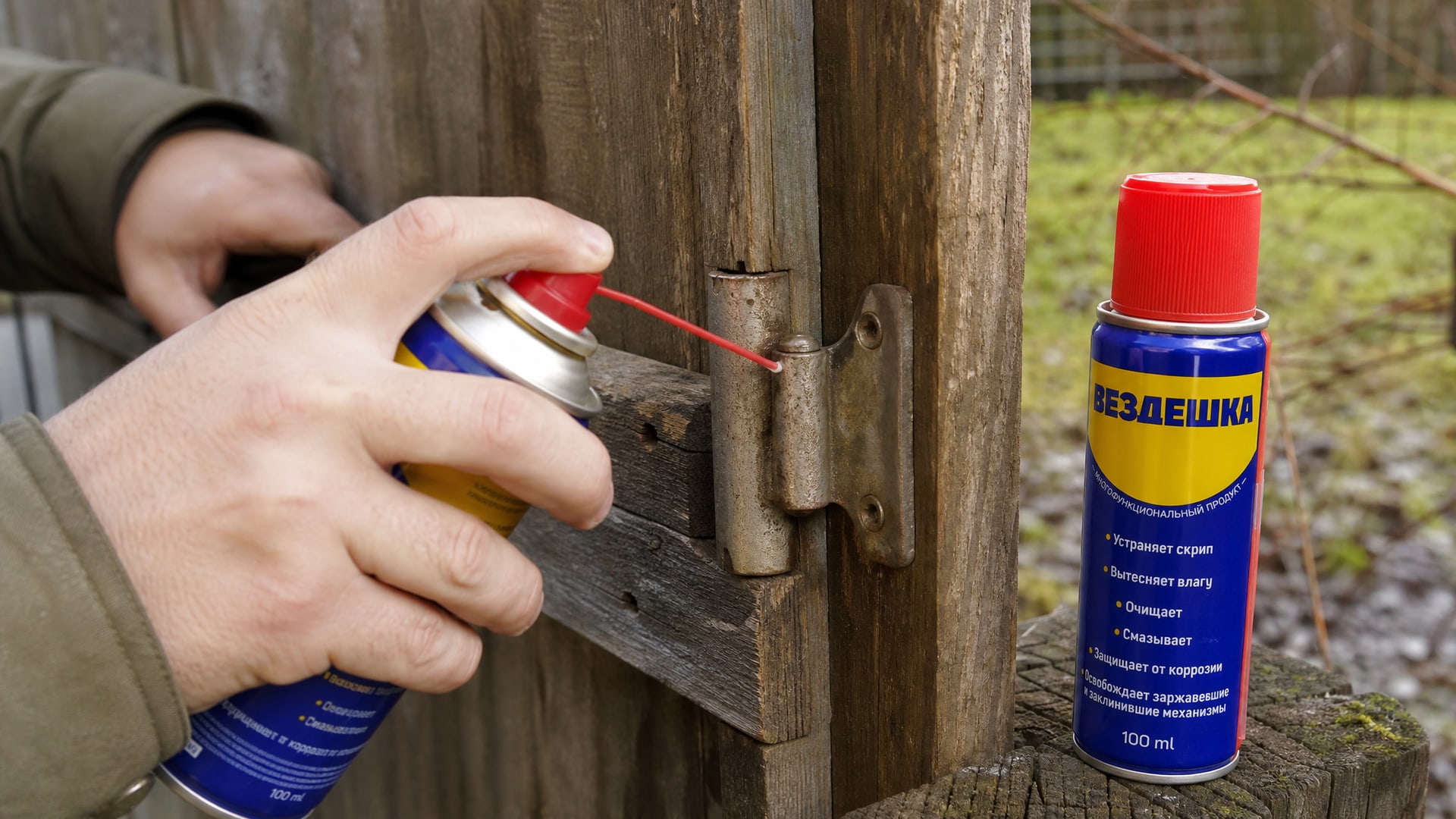Рука наносит универсальную смазку wd-40 на петли калитки.