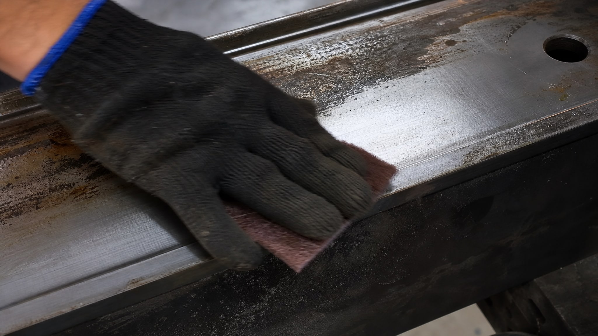 Рука в перчатке зачищает металлическую поверхность перед нанесением адгезии смазки.