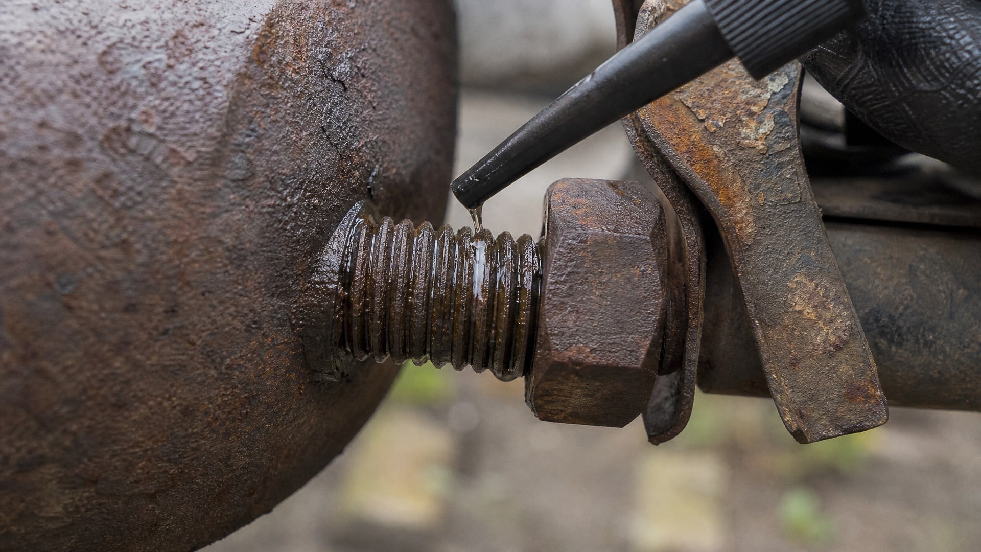 Капли WD40 проникают в заржавевшую резьбу болта глушителя.