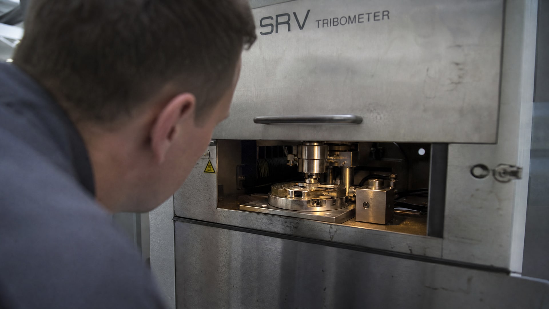 Техник изучает поверхность образца внутри трибометра SRV, оценивая несущую способность.
