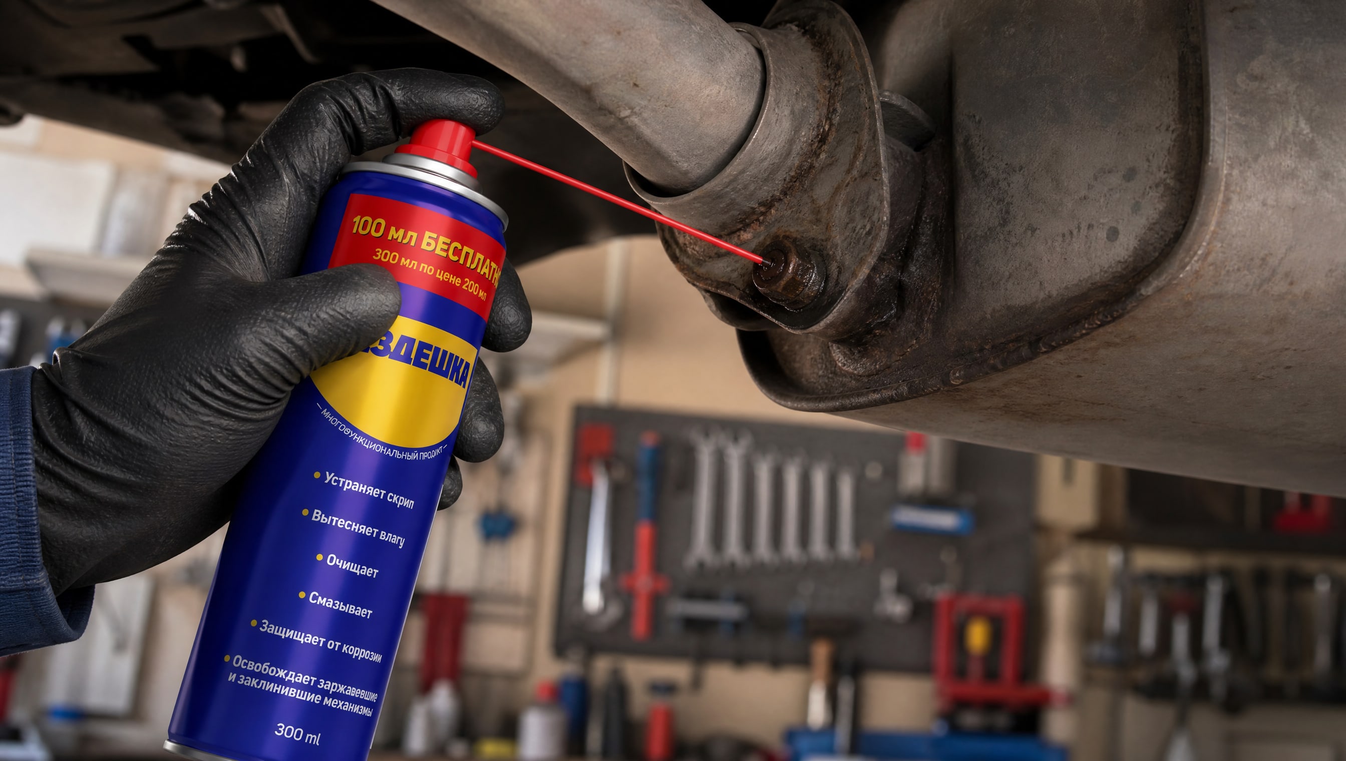 Рука в перчатке наносит универсальную смазку wd-40 на болты глушителя.