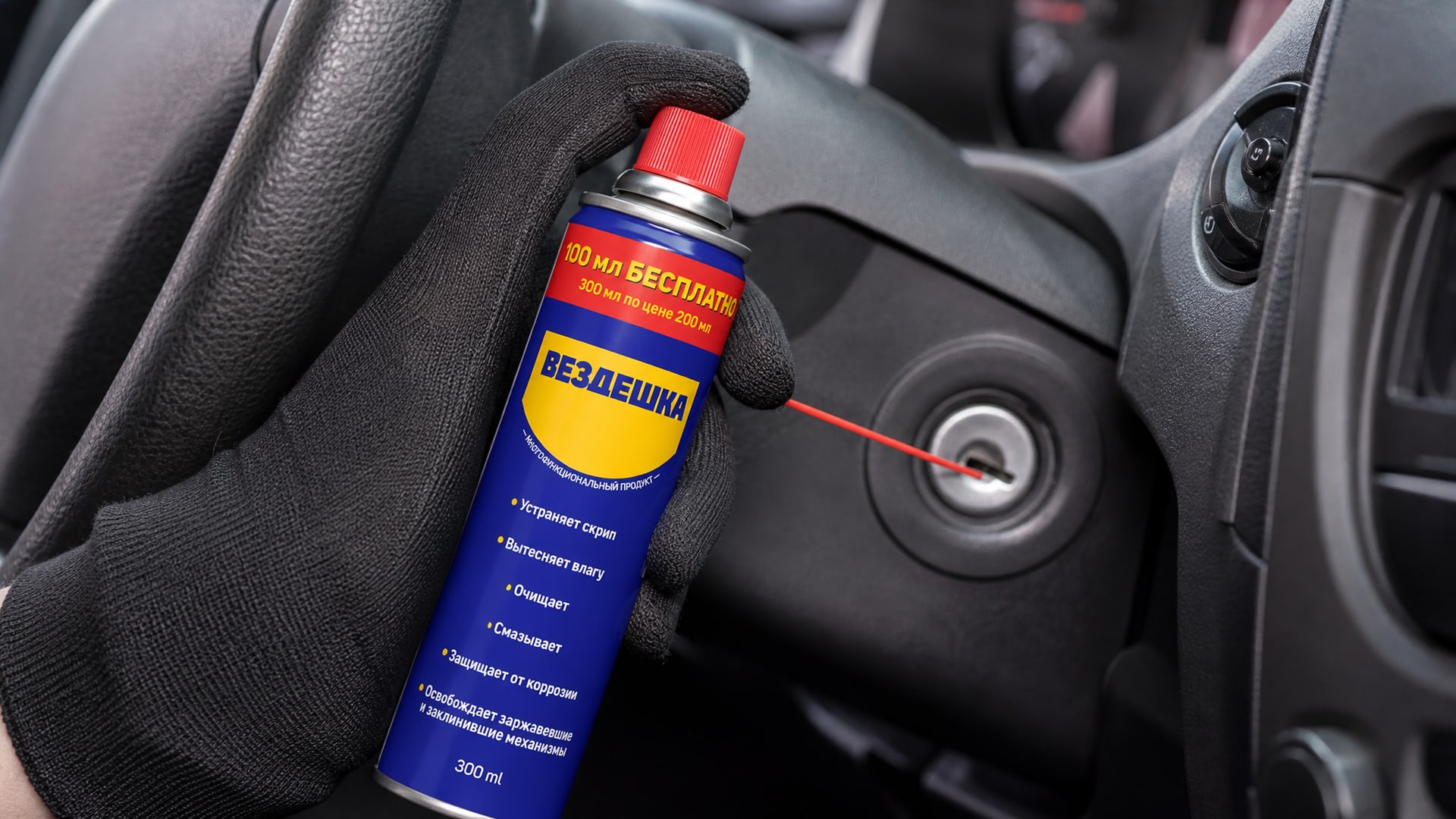 Рука в перчатке наносит универсальную смазку WD-40 на замок зажигания.
