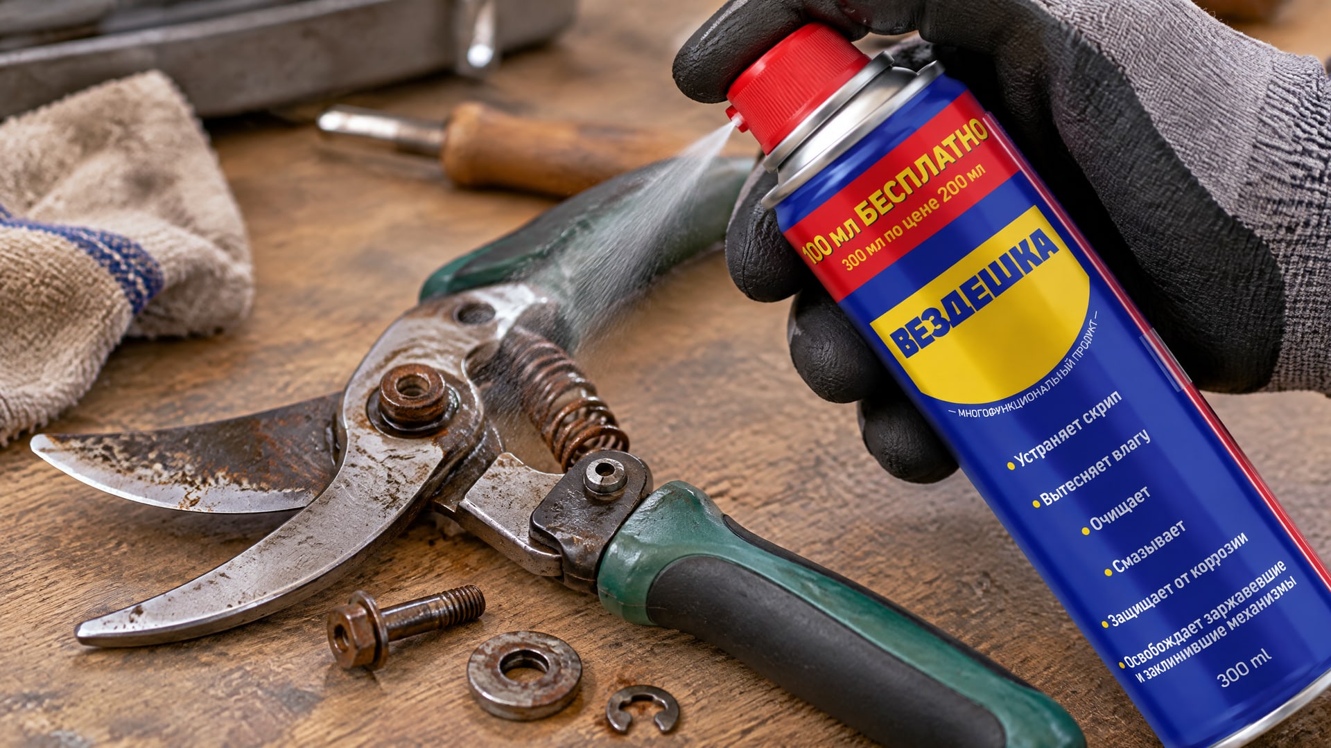 Рука в перчатке наносит универсальную смазку WD-40 на садовый инструмент.