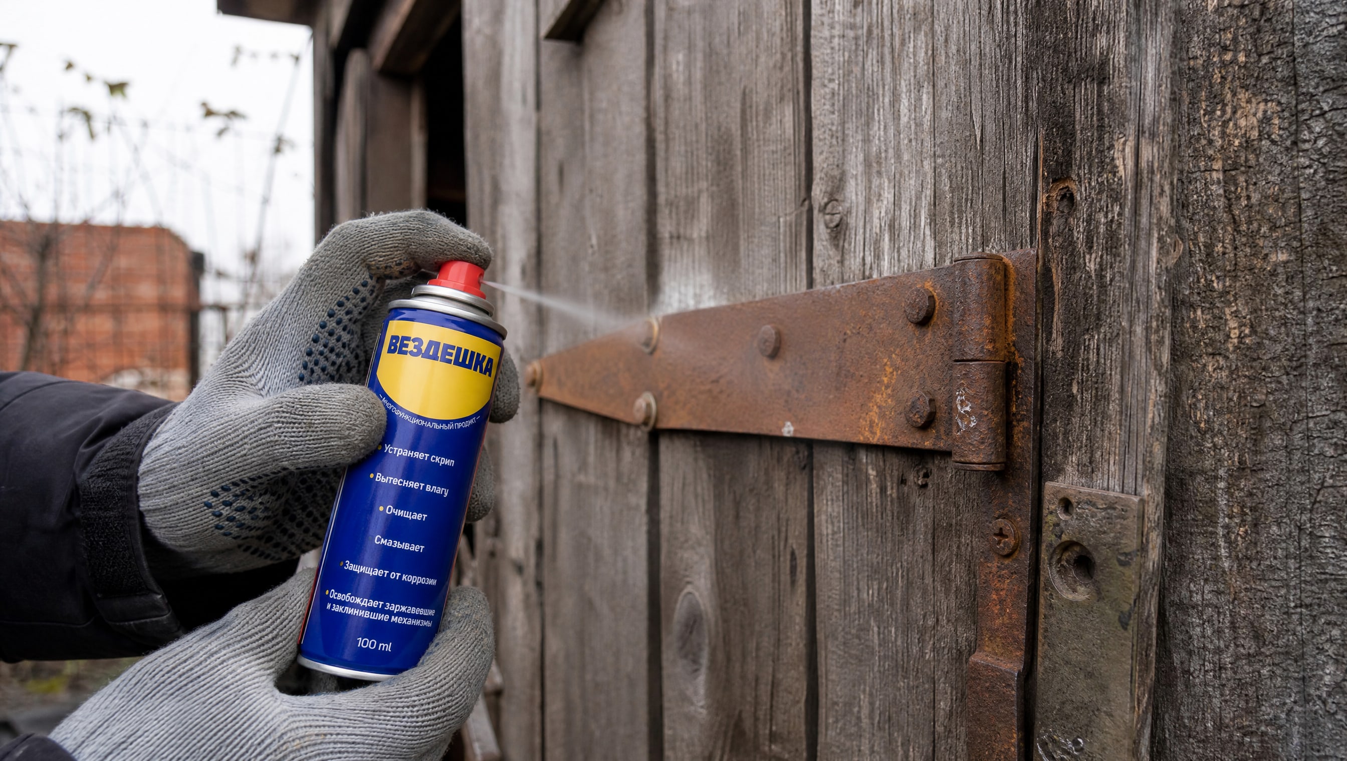 Рука в перчатке наносит универсальную смазку WD-40 на ржавые петли дверей